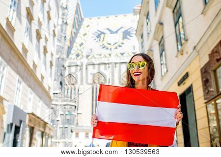 Young smiling woman holding austrian flag with the roof eagle emblem on the background in Vienna