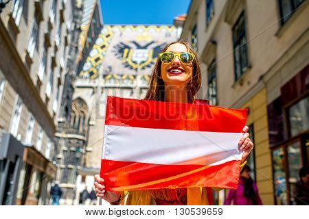 Young smiling woman holding austrian flag with the roof eagle emblem on the background in Vienna