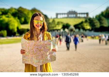 Young female tourist traveling with paper map in Schoenbrunn palace with Gloriette building on the background