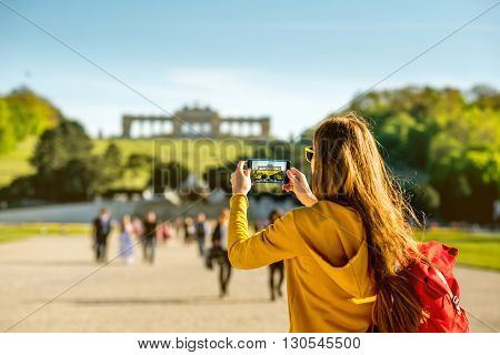 Young female tourist photographing with phone Gloriette building in Schoenbrunn palace in Vienna