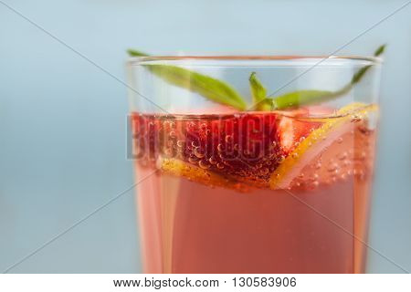 Glass of strawberry lemonade with pieces of strawberry, lemon and fresh mint. Closeup of mojito with beach on background. Fresh summer bright strawberry cocktail.