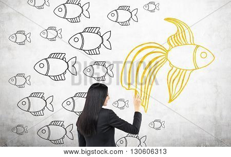 Different direction concept with businesswoman drawing goldfish sketch on concrete wall