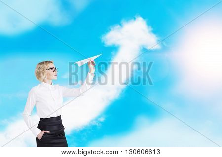 Success concept with businesswoman playing with paper plane on sky background with upward arrow cloud
