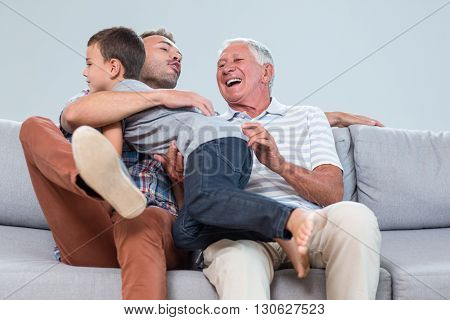 Father sitting on sofa with grandfather and embracing son in living room