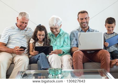 Happy family sitting on sofa using a laptop, digital, tablet, mobile phone in living room
