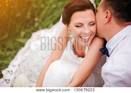 Closeup bride smiling while groom whispering compliments to her.