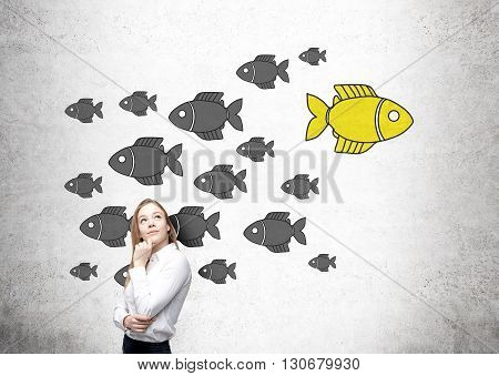 Different direction concept with thoughtful businesswoman and goldfish sketch on concrete wall