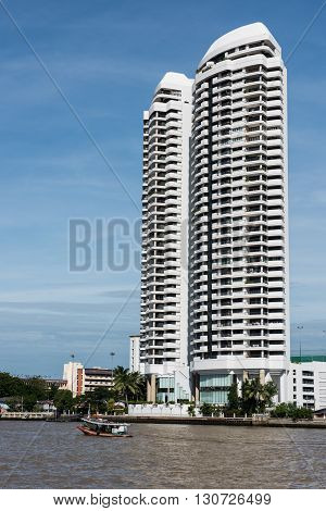 A tall standing, fabulously designed skycrapper in Minsk city on a clear, bright and sunny day. The Svislasch river in front of the skyscrapper is seen with travelers boating on the sunny day.