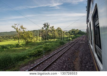 View from a running train while travelling to Bangkok. On the background, lush green fields and mountains are seen on a clear, bright day. Rail is an important transportation mode in Bangkok.