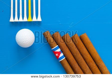 Detail of luxury Cuban cigars and golf equipments on the blue wooden desk