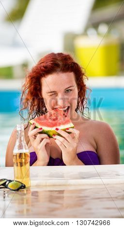 Young ginger curly girl wink on piscine with slices of watermelon and drinks 
