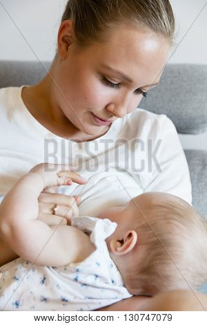 Portrait of a loving mother in sofa breastfeeding baby girl. Newborn child fed with breast milk by mom.