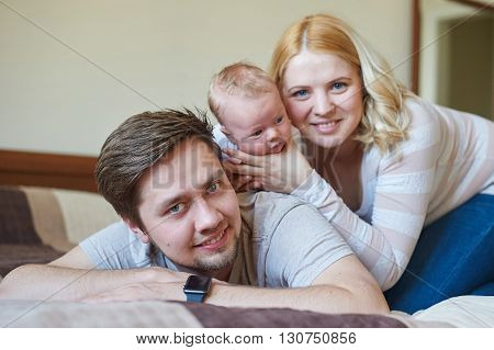 Beautiful happy couple and their baby relaxing in a bed together.