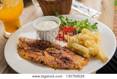 Fish steak in White plateGlass of waterFrench friesOrange juice placed on wooden table.