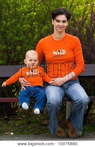 Baby and mother are having fun togather in the citypark on a sunny spring afternoon. They are wearing a similar orange T-shirt.