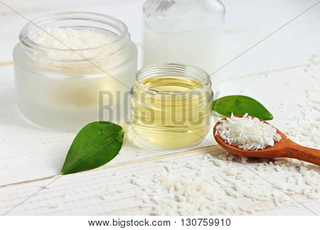 Coconut oil jar, coconut shavings spoon, fresh plant, white table. Natural skincare beneficial products.