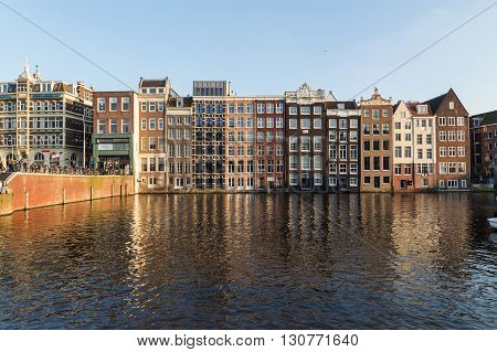AMSTERDAM NETHERLANDS - 17TH FEBRUARY 2016: Old Buildings along the Damrak in Amsterdam during the day. People can be seen.