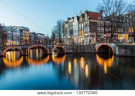 A view of the bridges at the Leidsegracht and Keizersgracht canals intersection in Amsterdam at dusk.