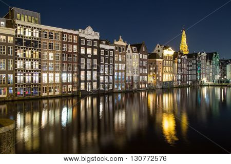 Old Buildings along the Damrak in Amsterdam at night. Reflections can be seen in the water.
