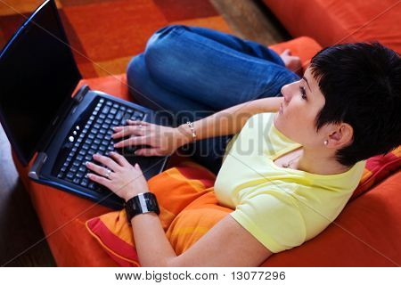 Ung kvinna använder en bärbar dator är hennes bekvämt vardagsrum.