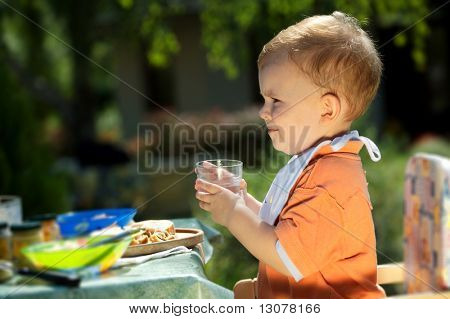 Two years old baby boy drinking. Family BBQ party outdoor, in the garden.