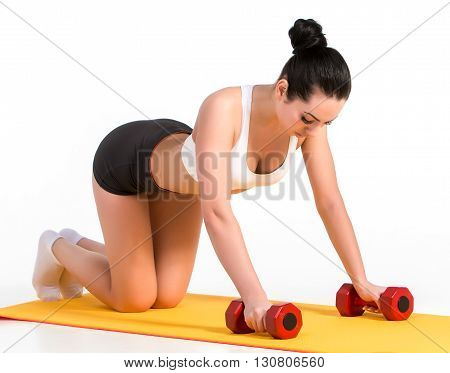 Strong young woman doing push ups exercise with dumbbells. Fitness model doing intense training on an yellow mat.