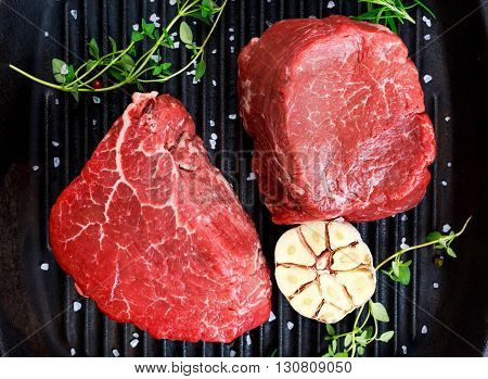 Fresh close up Raw Beef Filet steak with thyme, garlic, salt on grilled pan