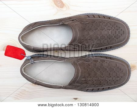 Brown pair of suede men's summer shoes with red price tag on wooden background