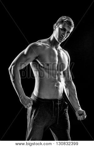 Strong bodybuilder man posing with perfect abs, houlders, biceps, triceps and chest on black background. Black and white