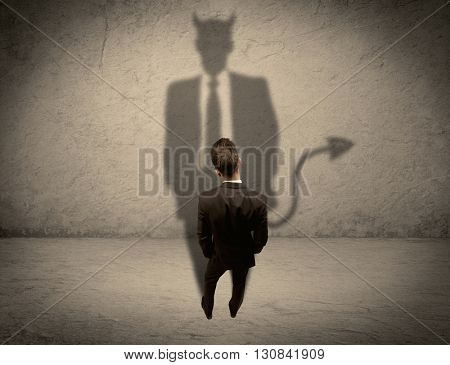 An experienced tricky businessman in suit looking at his devil desguise shadow reflected on the wall concept