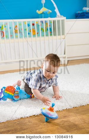 Baby boy ( 1 year old ) sitting on floor at home and playing with whirligig.