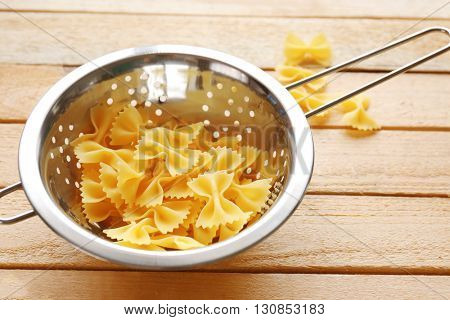 Pasta farfalle in  drainer on wooden table background
