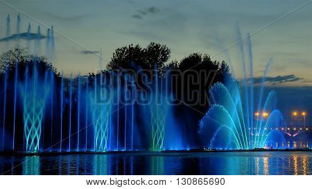 Amazing fantastic colorful fountain with bright illumination on the water pond or river with beautiful reflection at the evening or night. Beauty urban recreational concept.