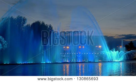 Amazing fantastic colorful fountain with bright illumination on the water pond or river with beautiful reflection at the evening or night. Beauty urban recreational concept.