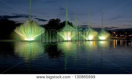 Amazing fantastic colorful fountain with bright illumination on the water pond or river with beautiful reflection at the evening or night. Beauty urban recreational concept.