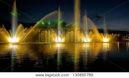 Amazing fantastic colorful fountain with bright illumination on the water pond or river with beautiful reflection at the evening or night. Beauty urban recreational concept.