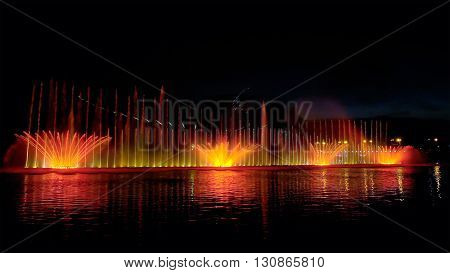 Amazing fantastic colorful fountain with bright illumination on the water pond or river with beautiful reflection at the evening or night. Beauty urban recreational concept.