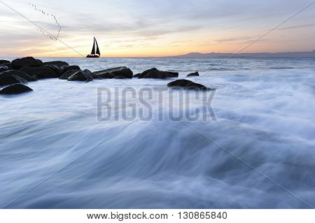 Sailboat silhouettesunset is a silhoueette of a sailboat with a white hot burning sun setting on the ocean horizon against a vivid orange sunset sky.