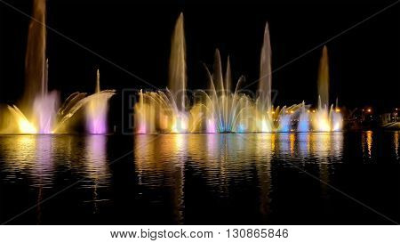 Amazing fantastic colorful fountain with bright illumination on the water pond or river with beautiful reflection at the evening or night. Beauty urban recreational concept.