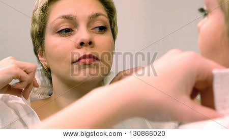 Blond business woman dresses and smartens up herself in front of mirror. Beauty and makeup concept.