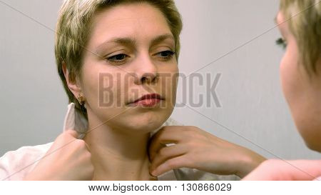 Blond business woman dresses and smartens up herself in front of mirror. Beauty and makeup concept.