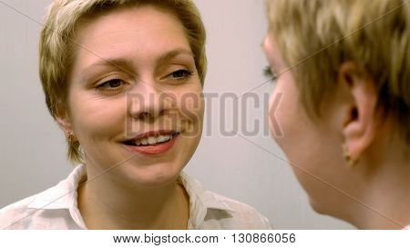 Blond business woman dresses and smartens up herself in front of mirror. Beauty and makeup concept.