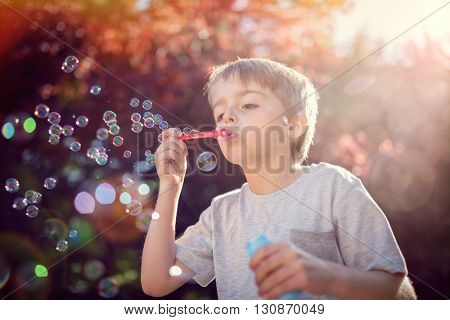 Little boy playing with bubble wand blowing soap bubbles in summer sunshine