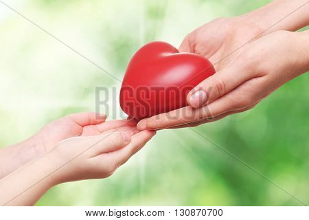Heart in child and mother hands on green nature background. Concept of taking care, protection, helping and assistance