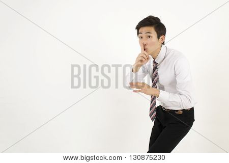 Asian young businessman placing finger on lips as if to say, shhhhh, be quiet, silence