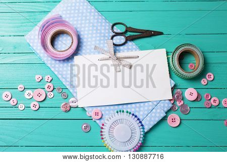 Sewing thread - buttons scissors fabric and empty tag on turquoise wooden background. Selective focus. Scrapbboking. Flat lay. Place for text.