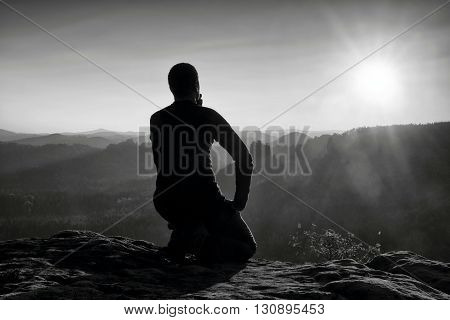 Sportsmann Hiker In Black Sportswear Sit On Mountain Top And Take A Rest. Tourist  Watch Down To Mor