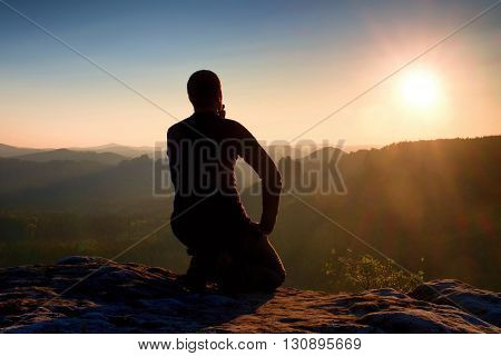 Sportsmann Hiker In Black Sportswear Sit On Mountain Top And Take A Rest. Tourist  Watch Down To Mor