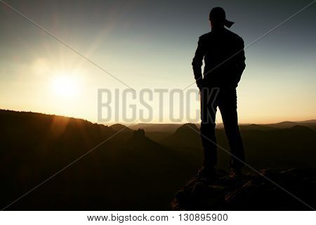 Hiker In Long Cap On Rock Empire And Watching To Sun. Beautiful Moment The Miracle Of Nature