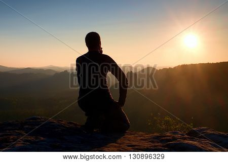 Sportsmann Hiker In Black Sportswear Sit On Mountain Top And Take A Rest. Tourist  Watch Down To Mor